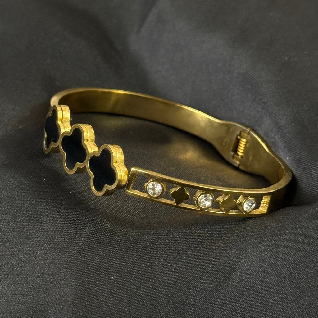 Gold bracelet with clover and gemstone designs on a dark fabric background